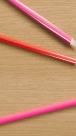 Vertical-Video-Of-Multi-Coloured-Pencils-Rolling-Down-Wooden-Background